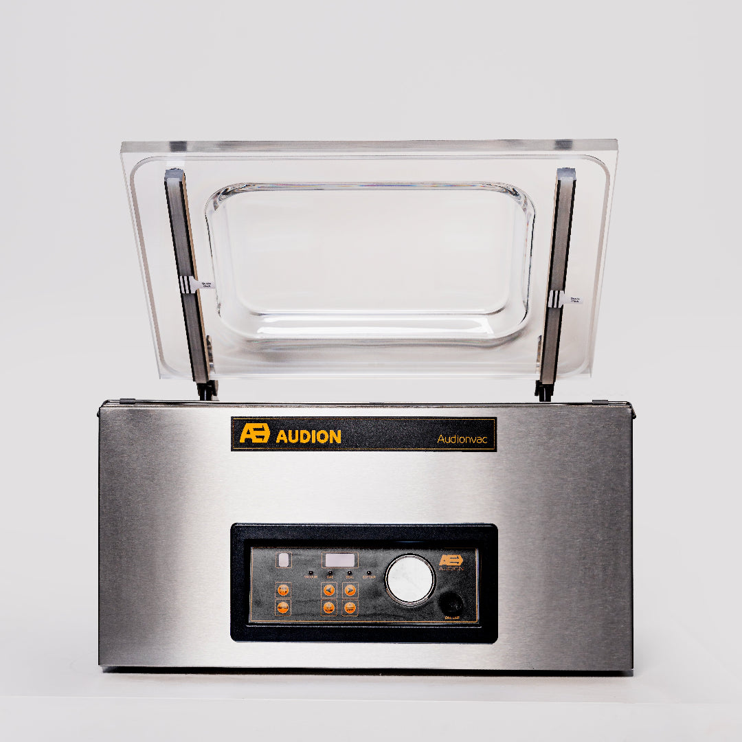 A Audion benchtop vacuum packer with a clear acrylic lid, digital control panel, and stainless steel body.