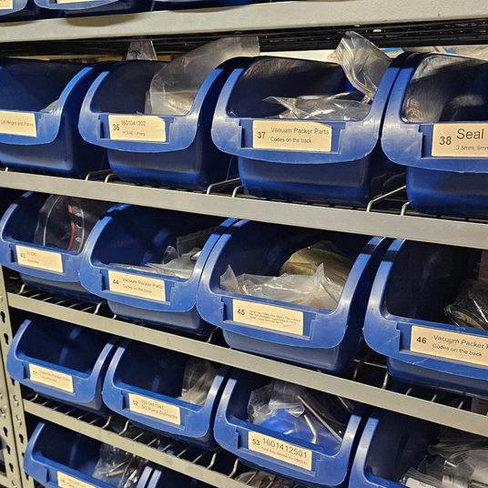 Shelving unit with blue storage bins labeled on a warehouse or storage facility.