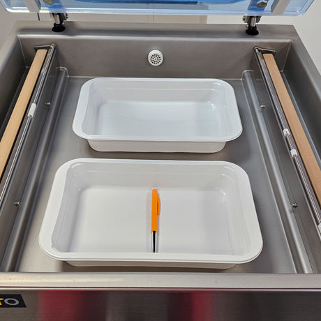 Two white containers with an orange tool inside a vacuum sealing machine.