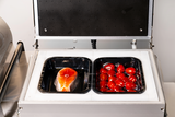 Two trays with food items inside a white appliance on a white background